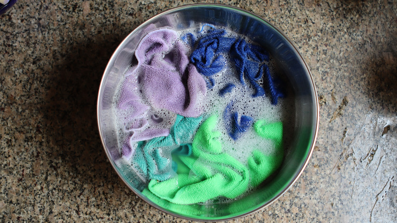 A bunch of colored microfiber towels soaking in a bucket of soapy water