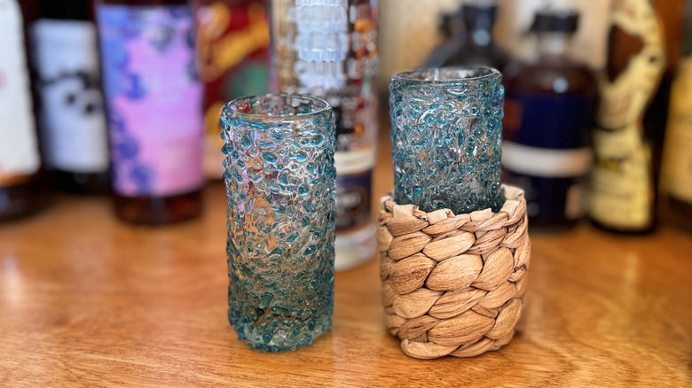 Two blue shot glasses sitting on a wooden table, with one inside of a napkin ring holder.