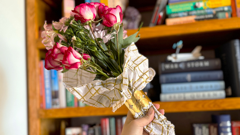 Someone holding a bouquet or roses and filler plants wrapped in checkered paper and a ring.