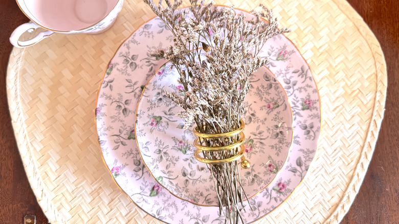 A pink floral China set sitting on a straw placemat with a flower bunch at the center.