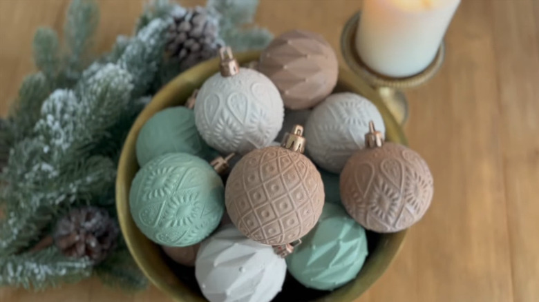 Ornaments with raised designs sit in a bowl on a wooden table