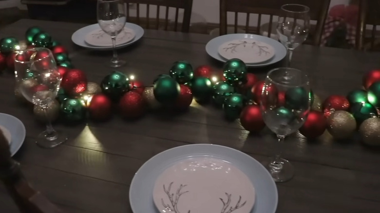 Lit up centerpiece made of ornaments stretching across the dinner table in front of plates