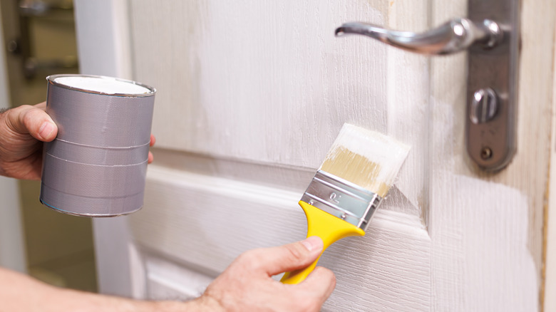 Person painting door white with paint brush