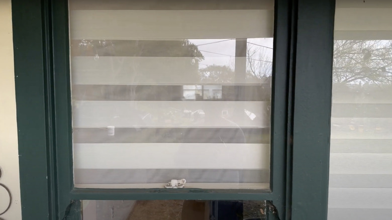 View of the inside of a home visible from outside through the sheer slats of zebra blinds.