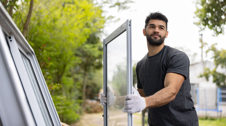 A handsome man wearing work gloves carries a window