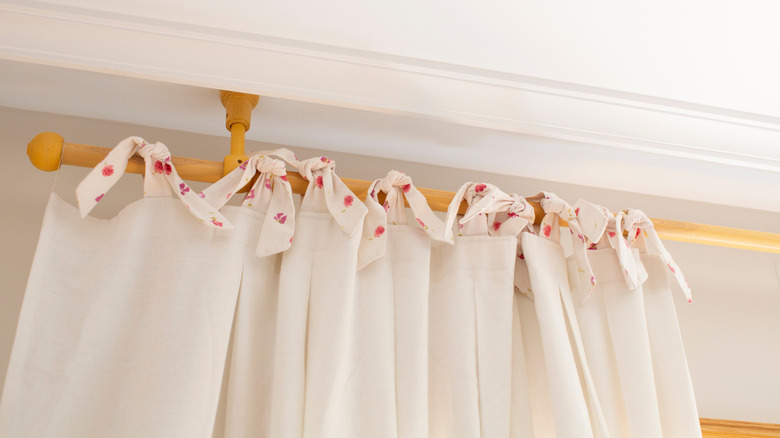 Wooden curtain rod holding white curtain with bows