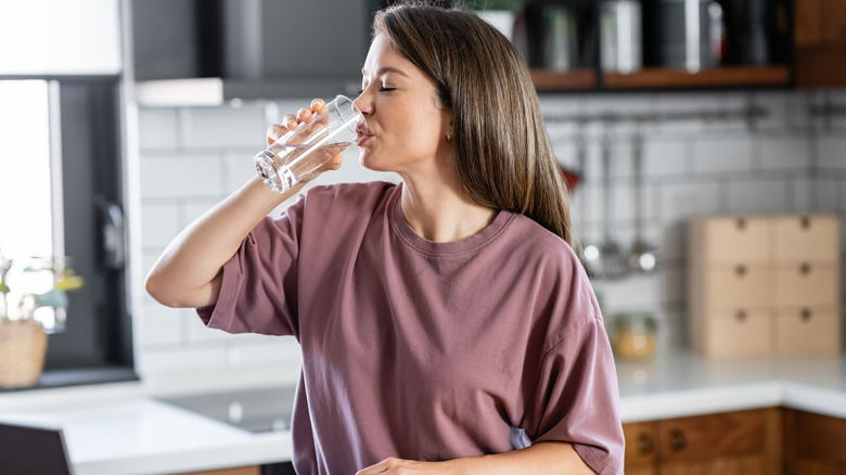 A cheerful woman drinks water from a glass in her kitchen