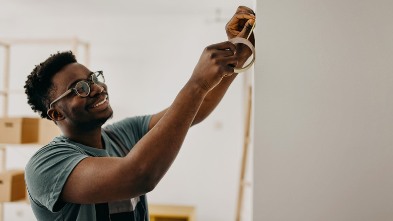 A smiling man places masking tape on a wall.