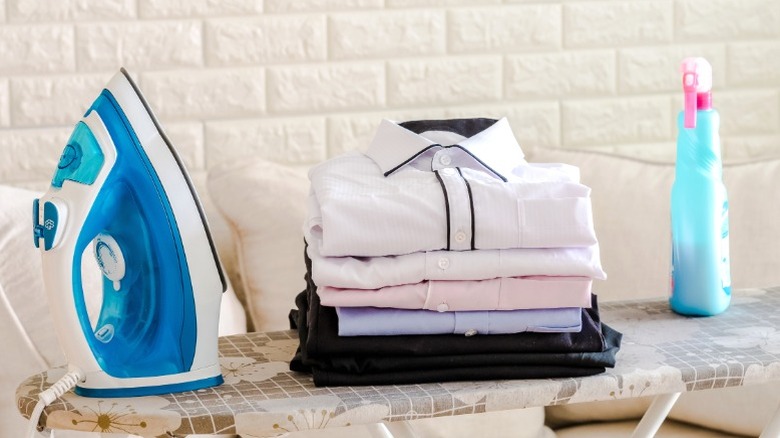 iron with folded clothes and spray starch on ironing board