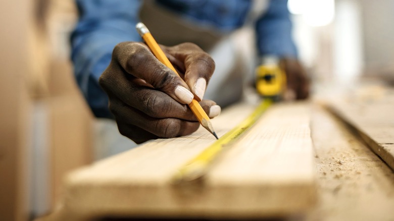 Man running measuring tape down 1-by-6 board and marking it with a pencil,