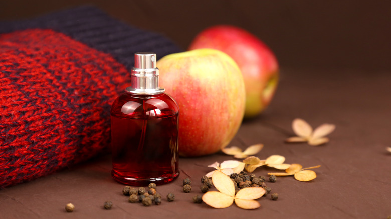 Red bottle of scent spray beside apples, peppercorns, and knit sweater