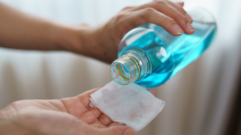 person putting rubbing alcohol on cloth