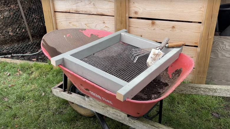 A DIY steel mesh and wood soil sifter sit snugly atop a wheelbarrow.