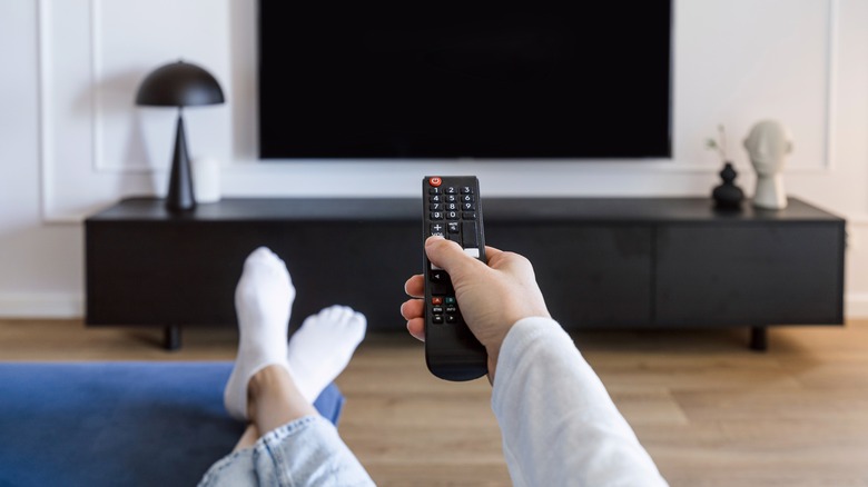 Person holding TV remote up to TV with feet up on ottoman