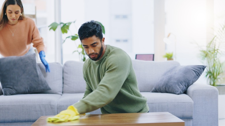 Man wiping down wooden table in living room