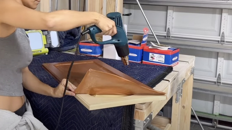 A woman removing thermofoil from cabinet with a heat gun