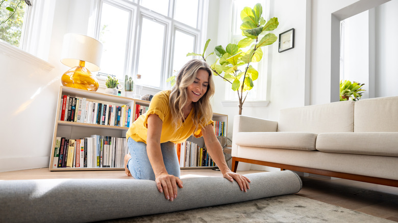 A woman is rolling out a new rug in your living room.