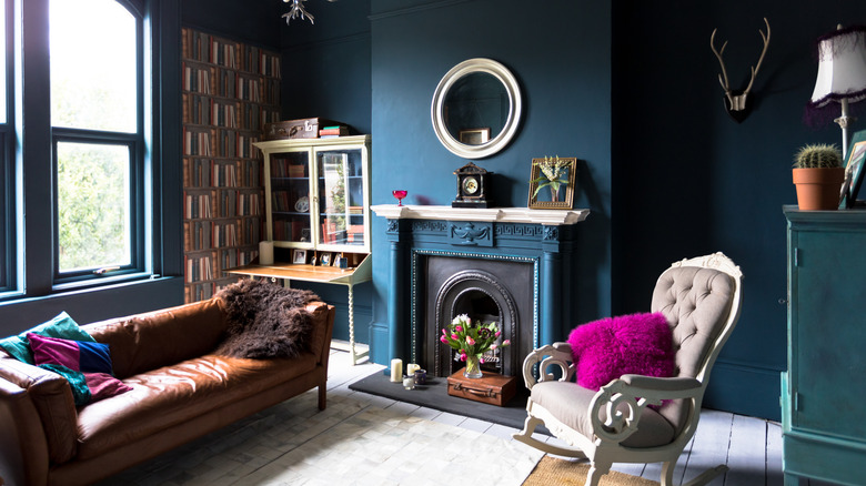 An eclectic living room with blue walls, brown leather couch, and pink fluffy pillow