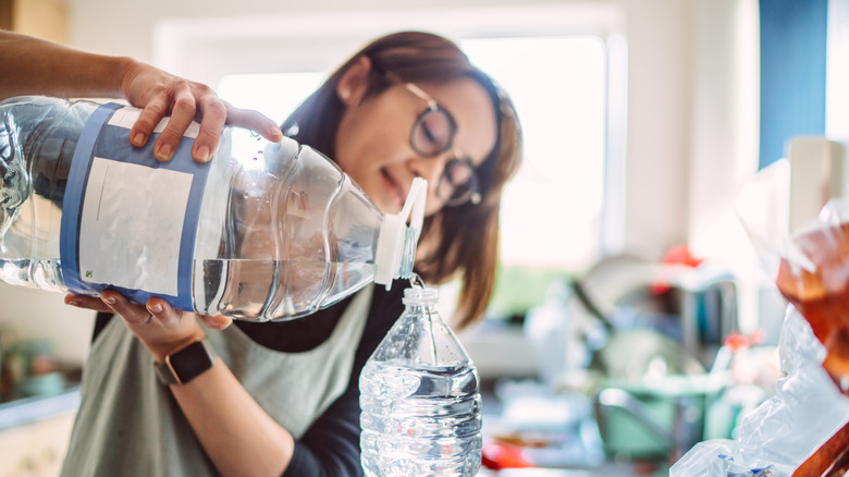 Woman pouring water out of plastic jug and into a smaller bottle