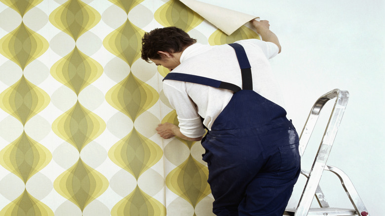 Man installing yellow patterned wallpaper