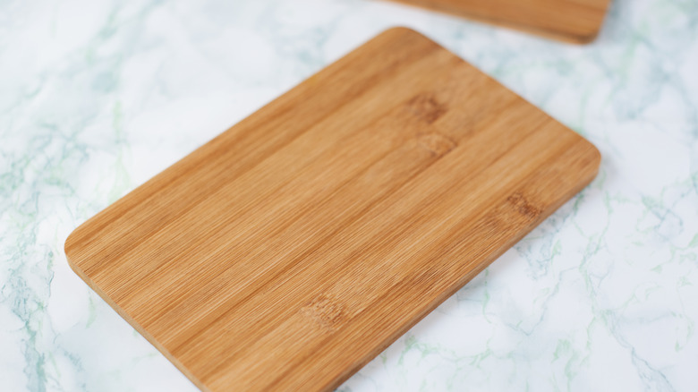 A rectangular bamboo cutting board sits on a white and gray marble counter.