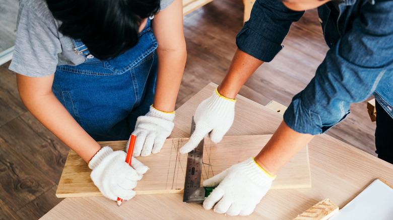 Two people measuring and marking wooden plank