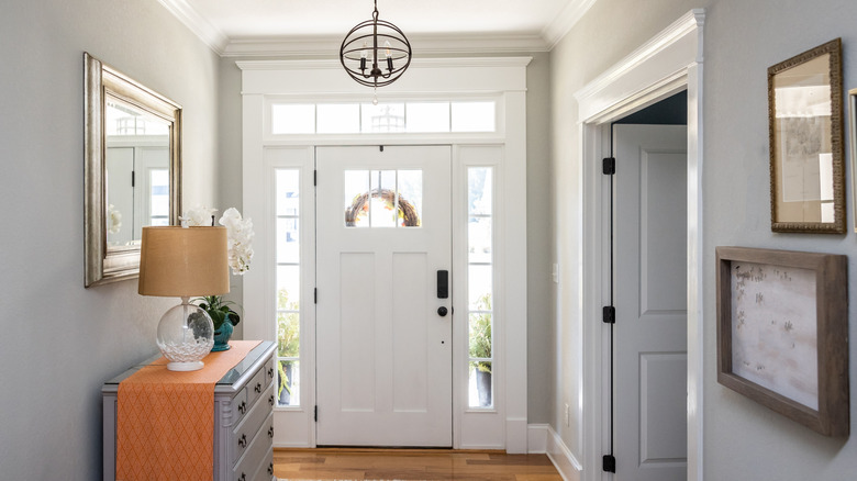 An open large and wide interior front door hallway foyer with transom, hanging light fixture, coastal colors and entry way table and wood floors.