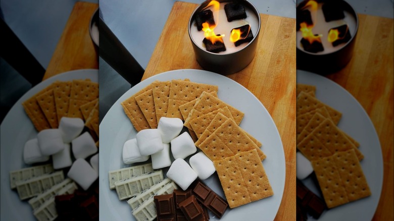 A portable firepit and s'mores station rest on a block of wood