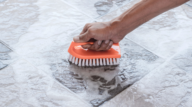 person's hand scrubbing tile floor