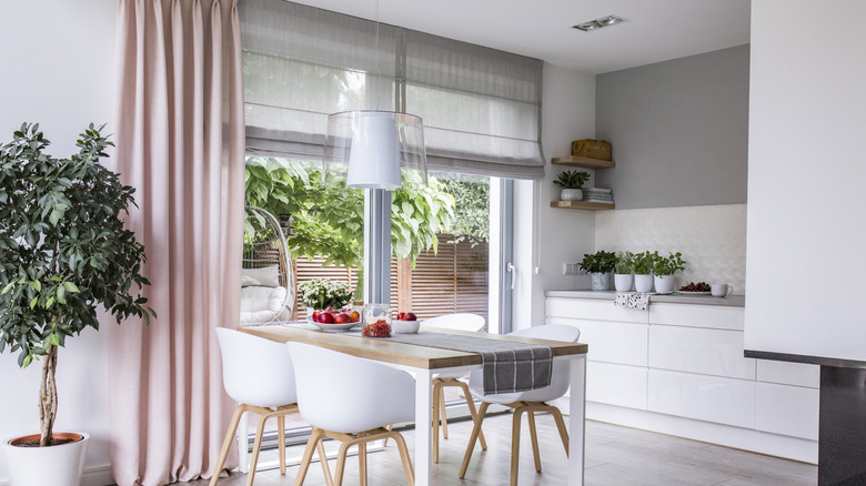 A white kitchen with a large sliding glass door with a shade and a pink curtain