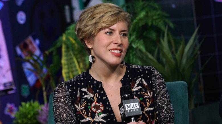 Erin Napier seated wearing a black printed dress with plants in the background