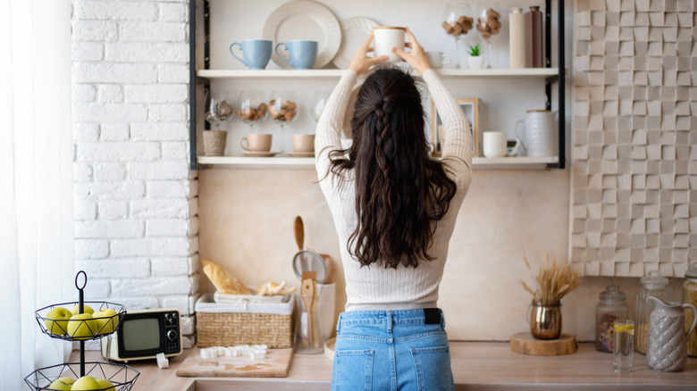 Woman placing coffee mug on decorated kitchen shelving