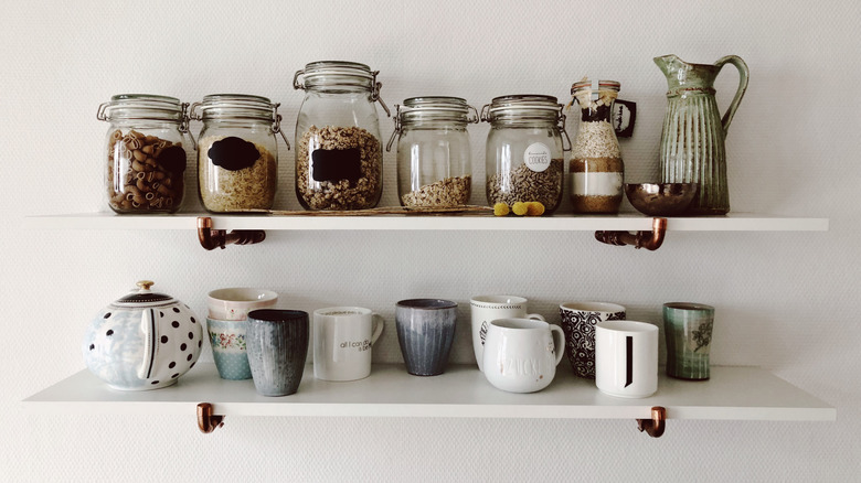 Coffee mugs and glass jars on two white floating shelves