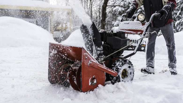 A person using a red two-stage snow blower