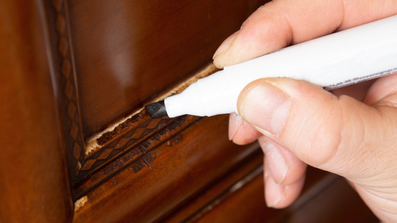 A person uses a touch-up marker to cover a damage on a wood furniture