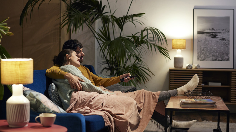 A woman and a man enjoying cozy lighting under a blanket on a couch