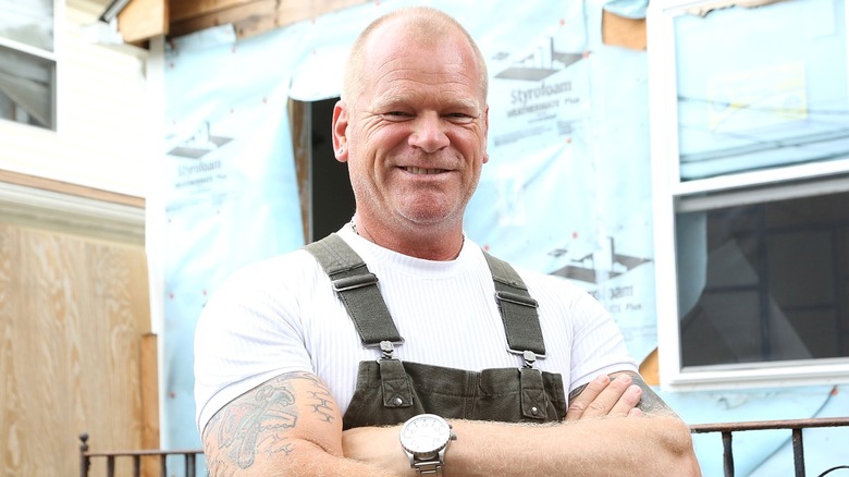 Mike Holmes smiling wearing overalls in front of home build