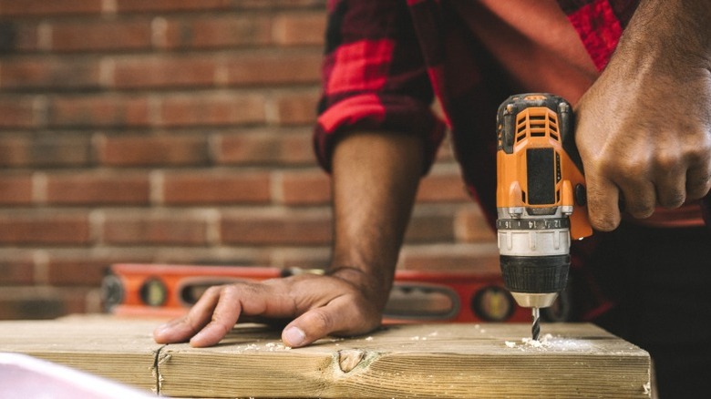 man in red flannel drilling hole in wood board