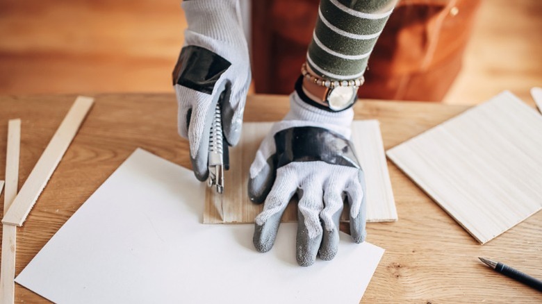 woman in cut gloves cutting wood strips with utility knife