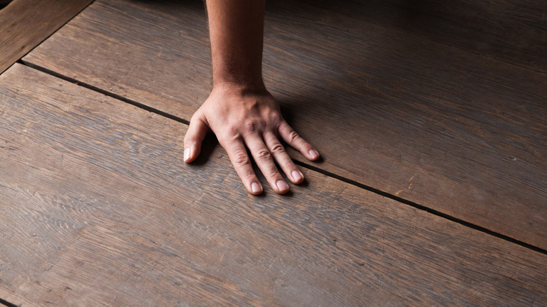 A hand touching an old hardwood floor