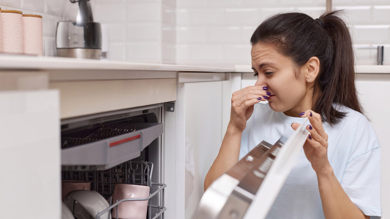 A woman plugs her nose while opening a dishwasher