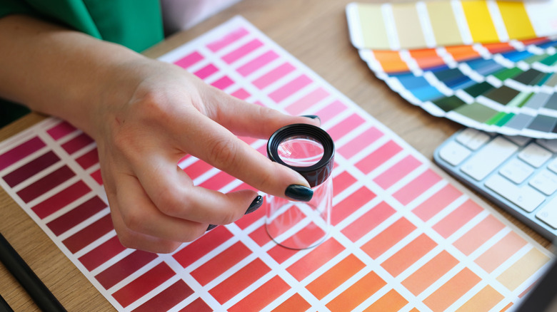 A hand holding a magnifying glass over color chips