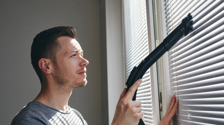 Man vacuuming the blinds