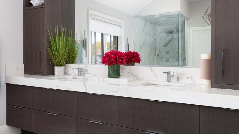 slab cabinets with brown wood finishing in modern bathroom with flowers and a mirror