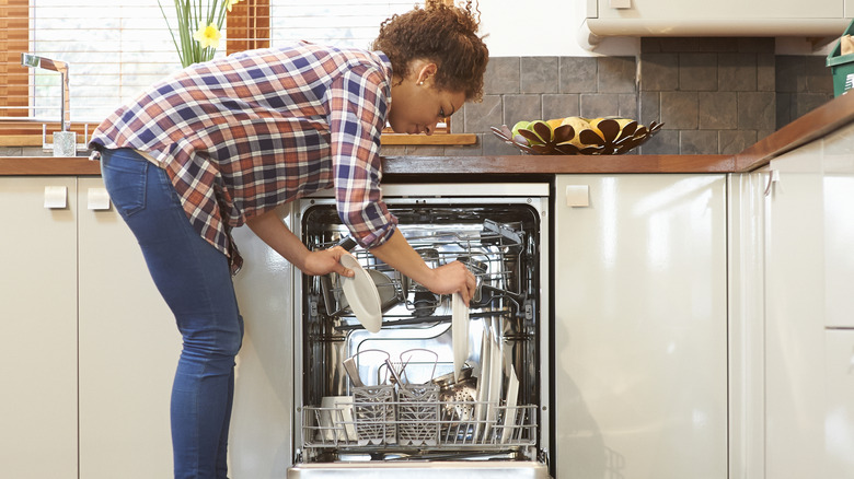 Woman in jeans loads dishwasher