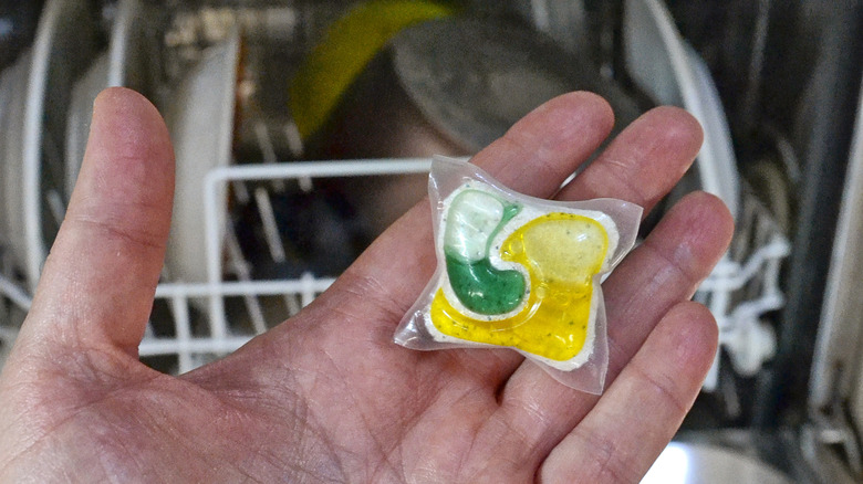 Person holding detergent tablet near dishwasher