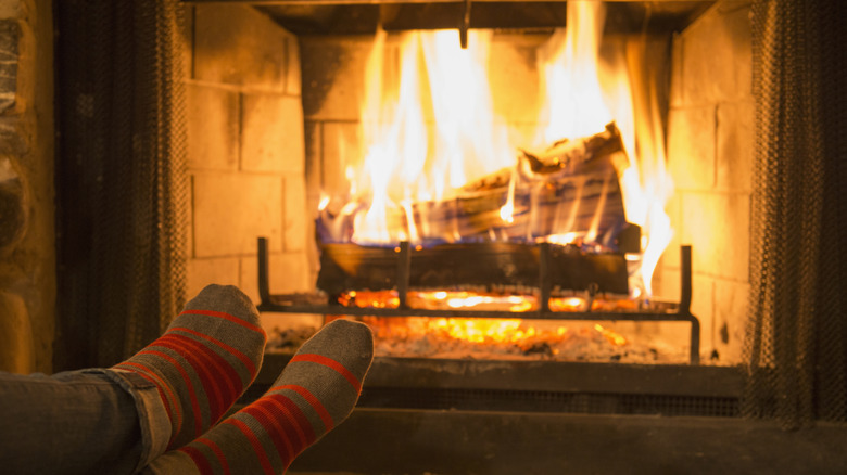 Person relaxing by a lit fireplace with a mesh curtain pulled back