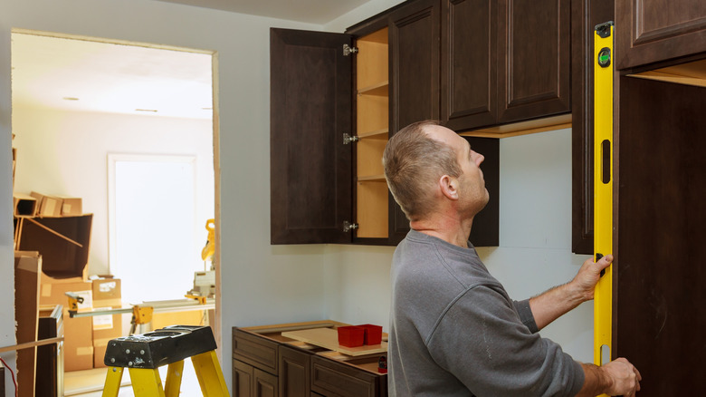 Man measuring upper kitchen cabinets.