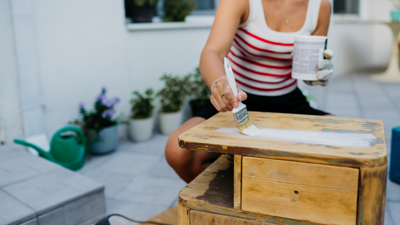 closeup of a woman painting a side table in white