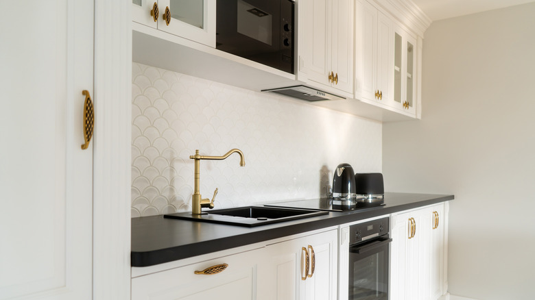 White kitchen with stylish gold and copper faucets and handles.